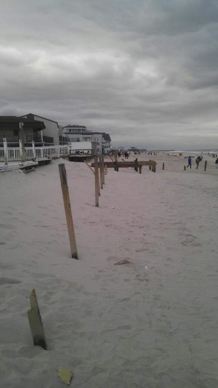 Cloudy beach with buildings and wooden posts.