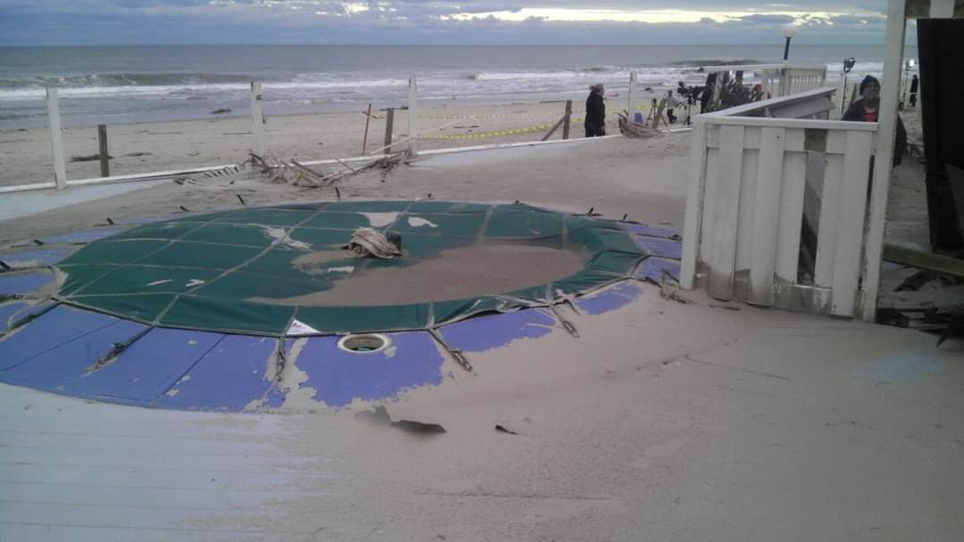 Beachfront pool covered in sand after storm.
