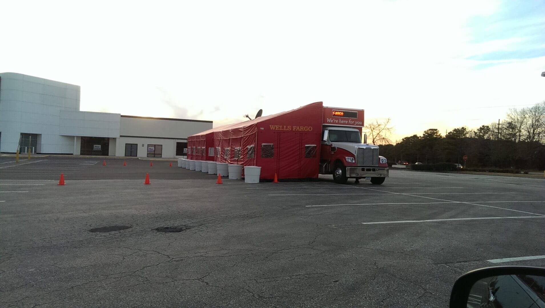 A large red food truck parked beside a building during sunset.